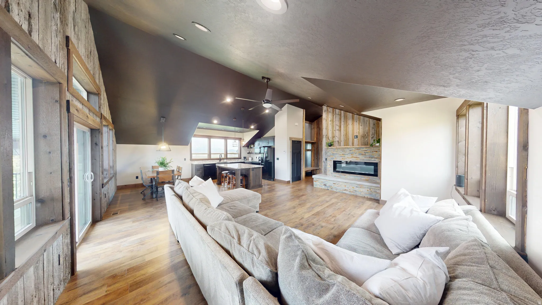 Living area with vaulted ceiling, light wood-type flooring, a stone fireplace, and a ceiling fan
