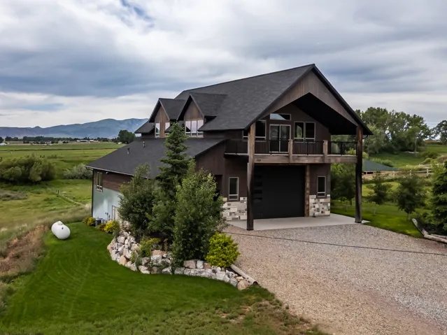 Modern rustic home featuring a dark wood siding exterior, stone accents, and a covered balcony