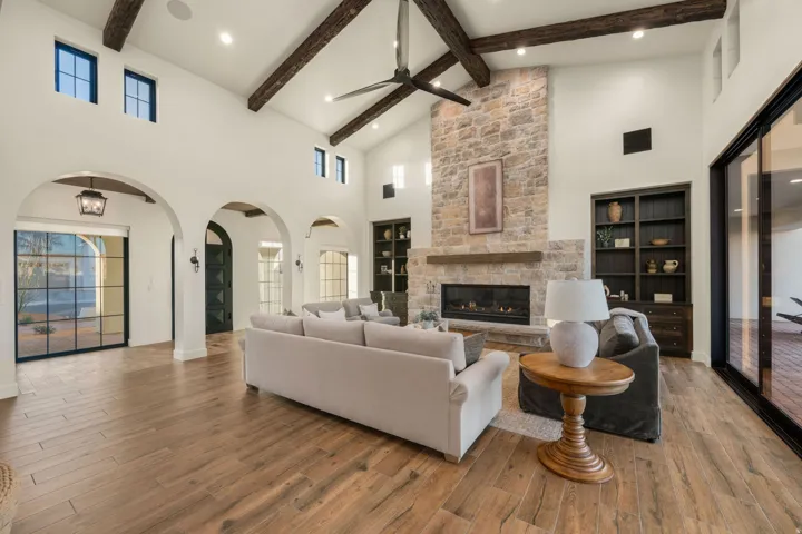 Living area with arched walkways, hardwood / wood-style floors, built in features, a ceiling fan, and a stone fireplace