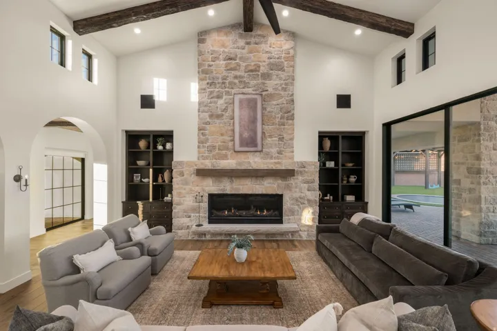 Living area with arched walkways, wood-type flooring, a stone fireplace, and vaulted ceiling