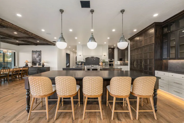 Kitchen with hanging light fixtures, a breakfast bar area, glass fronted cabinets, beam ceiling, and dark stone countertops