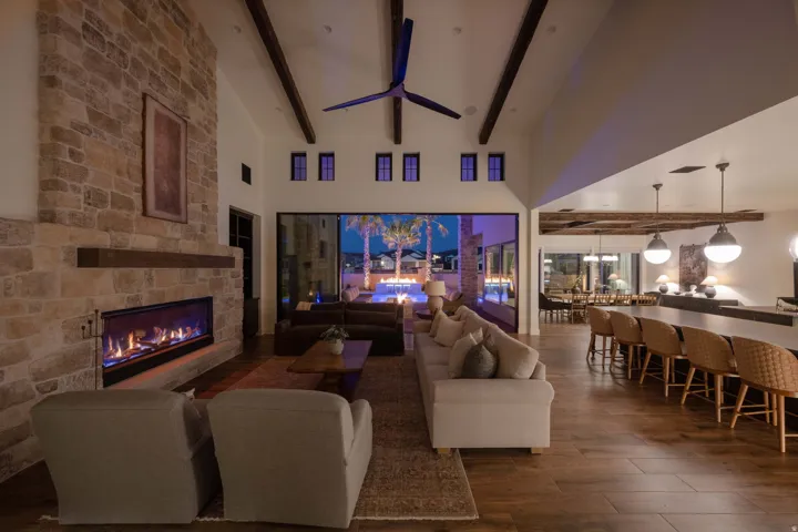 Living area with dark wood finished floors, a stone fireplace, a ceiling fan, and lofted ceiling