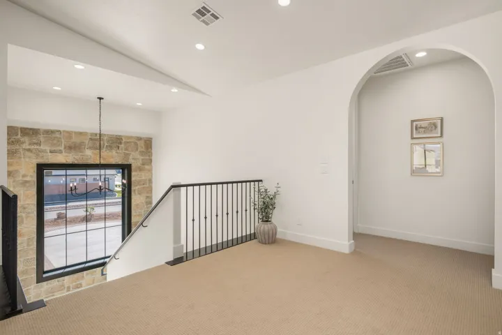 Empty room with light colored carpet, vaulted ceiling, arched walkways, and recessed lighting