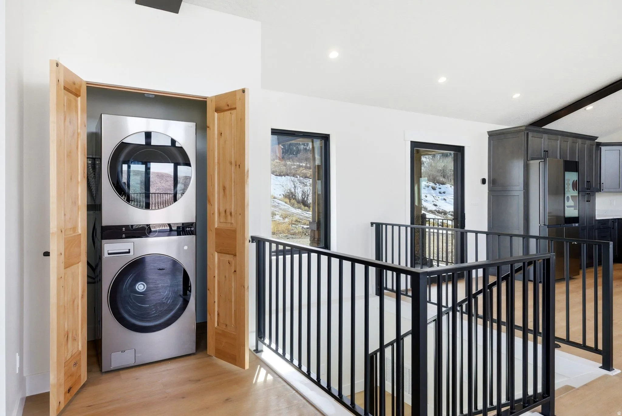 Laundry area with beam ceiling, stacked washer / drying machine, recessed lighting, and light wood-style flooring