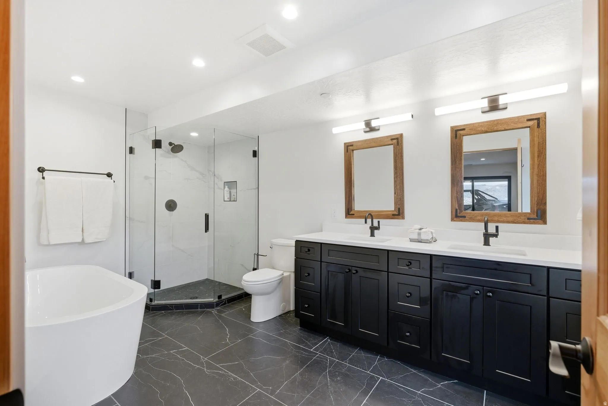 Bathroom with double vanity, a marble finish shower, a freestanding tub, recessed lighting, and dark marble finish flooring