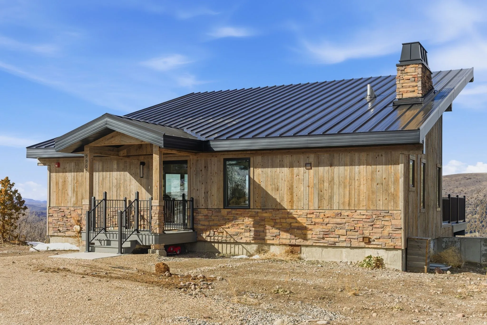 View of front of house featuring stone siding, covered porch, and a metal roof
