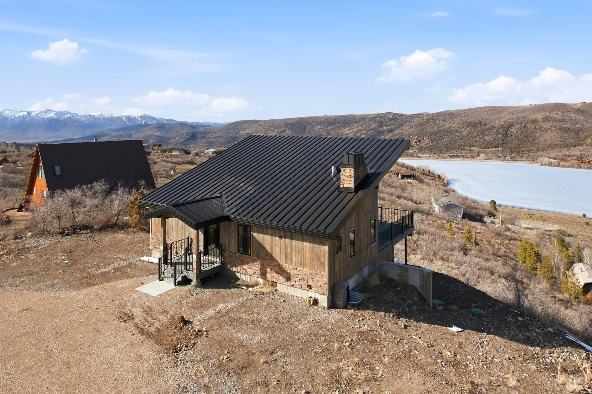 View of front of house with a mountain and lake views, a standing seam roof, a chimney, and stone siding