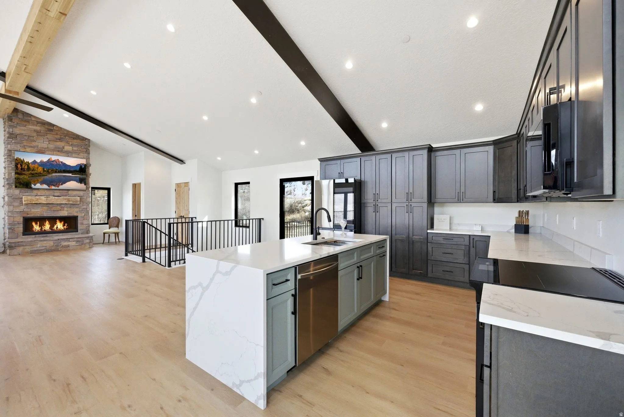 Kitchen featuring light stone counters, a center island with sink, open floor plan, vaulted ceiling, and black appliances