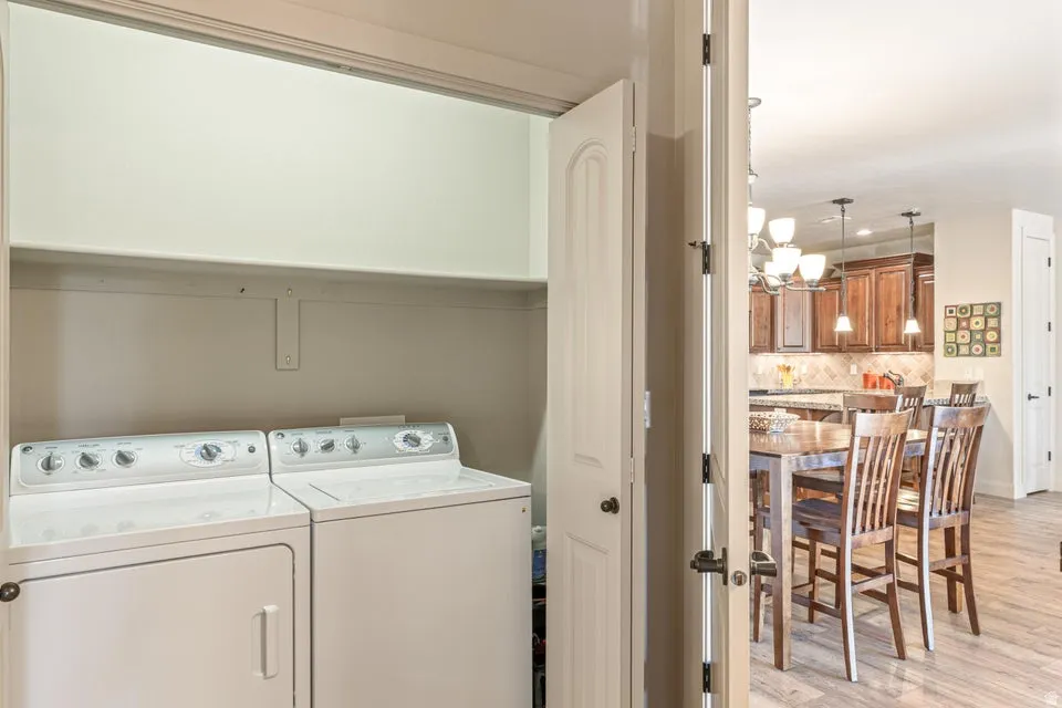 Laundry area with light wood-style floors, washer and clothes dryer, and hanging lights