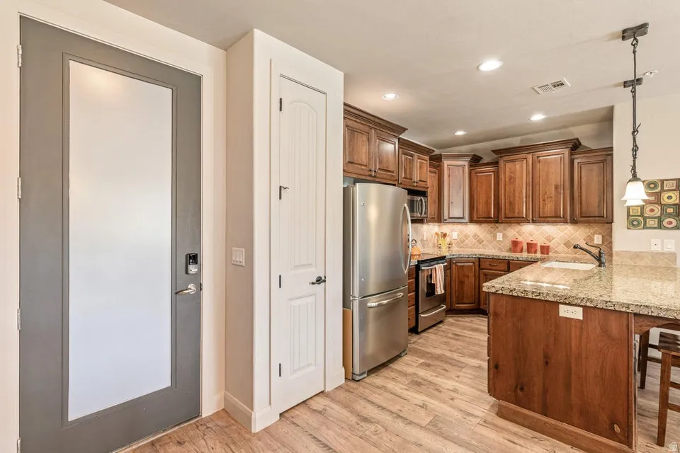 Kitchen featuring a peninsula, decorative light fixtures, stainless steel appliances, wood finish cabinetry, and a breakfast bar area