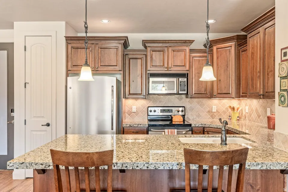 Kitchen featuring a kitchen bar, stainless steel appliances, light stone countertops, wood finish cabinets, and a peninsula