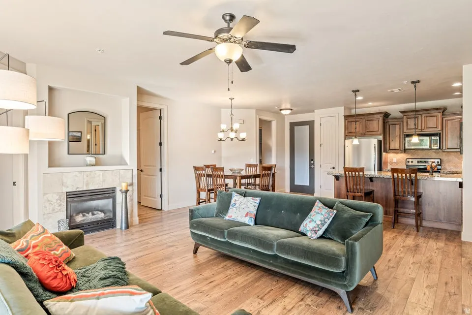 Living room with a tile fireplace, light wood finished floors, a ceiling fan, and hanging lights