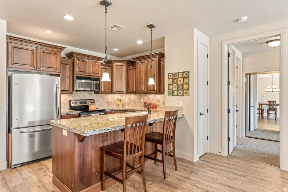 Kitchen featuring stainless steel appliances, wood finish cabinets, a peninsula, a kitchen breakfast bar, and light wood-style flooring
