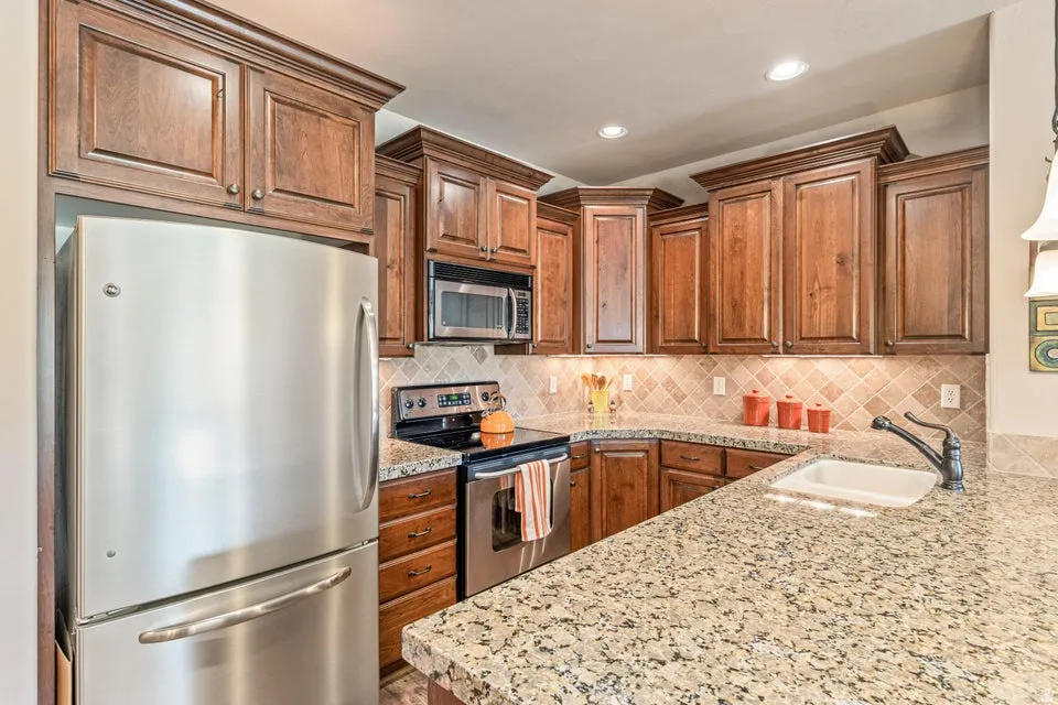 Kitchen featuring stainless steel appliances, wood finish cabinetry, tasteful backsplash, light stone counters, and recessed lighting