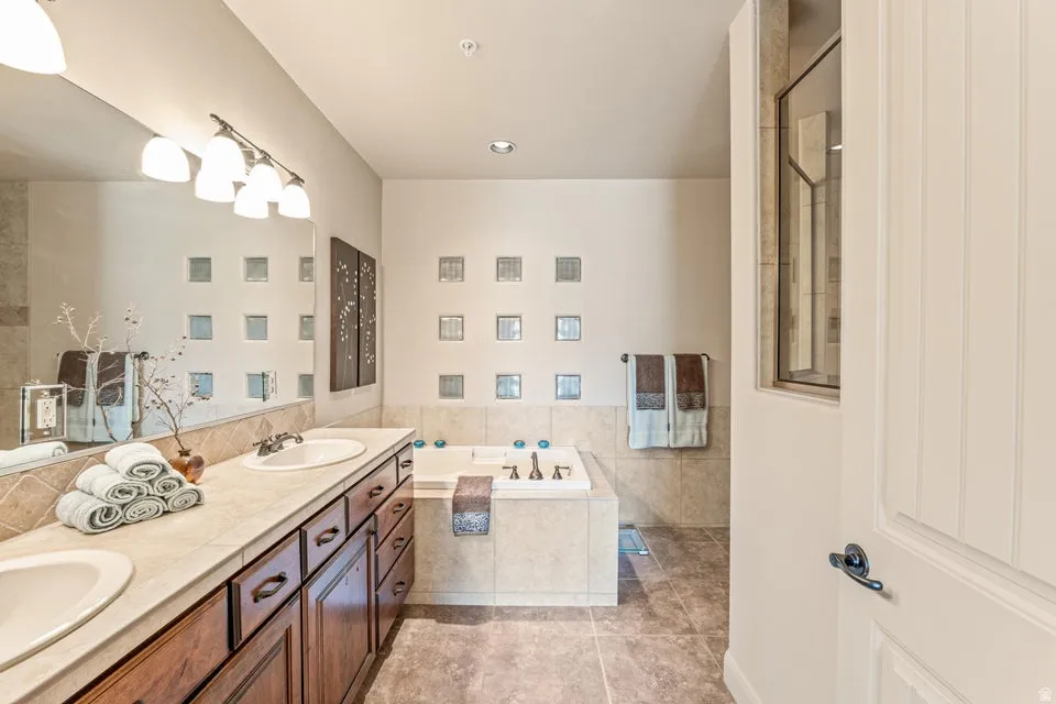 Bathroom featuring a garden tub, double vanity, tile walls, and light tile patterned floors