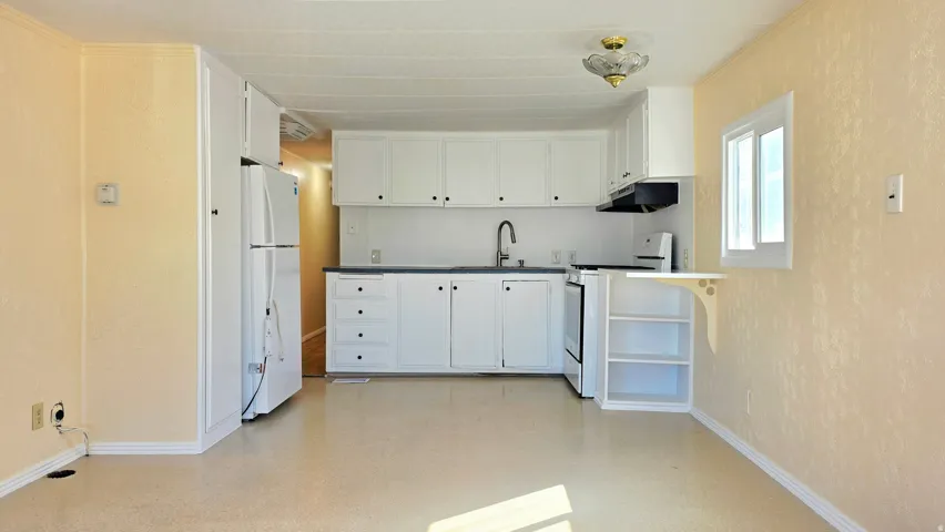 Kitchen with white cabinets, white appliances, and dark countertops