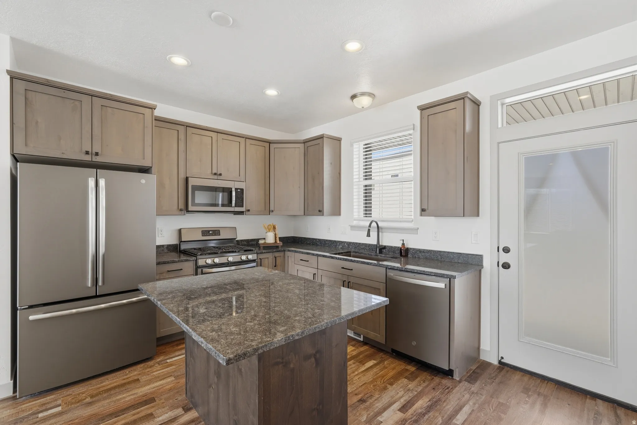 Kitchen featuring stainless steel appliances, dark stone counters, dark wood-type flooring, a center island, and recessed lighting