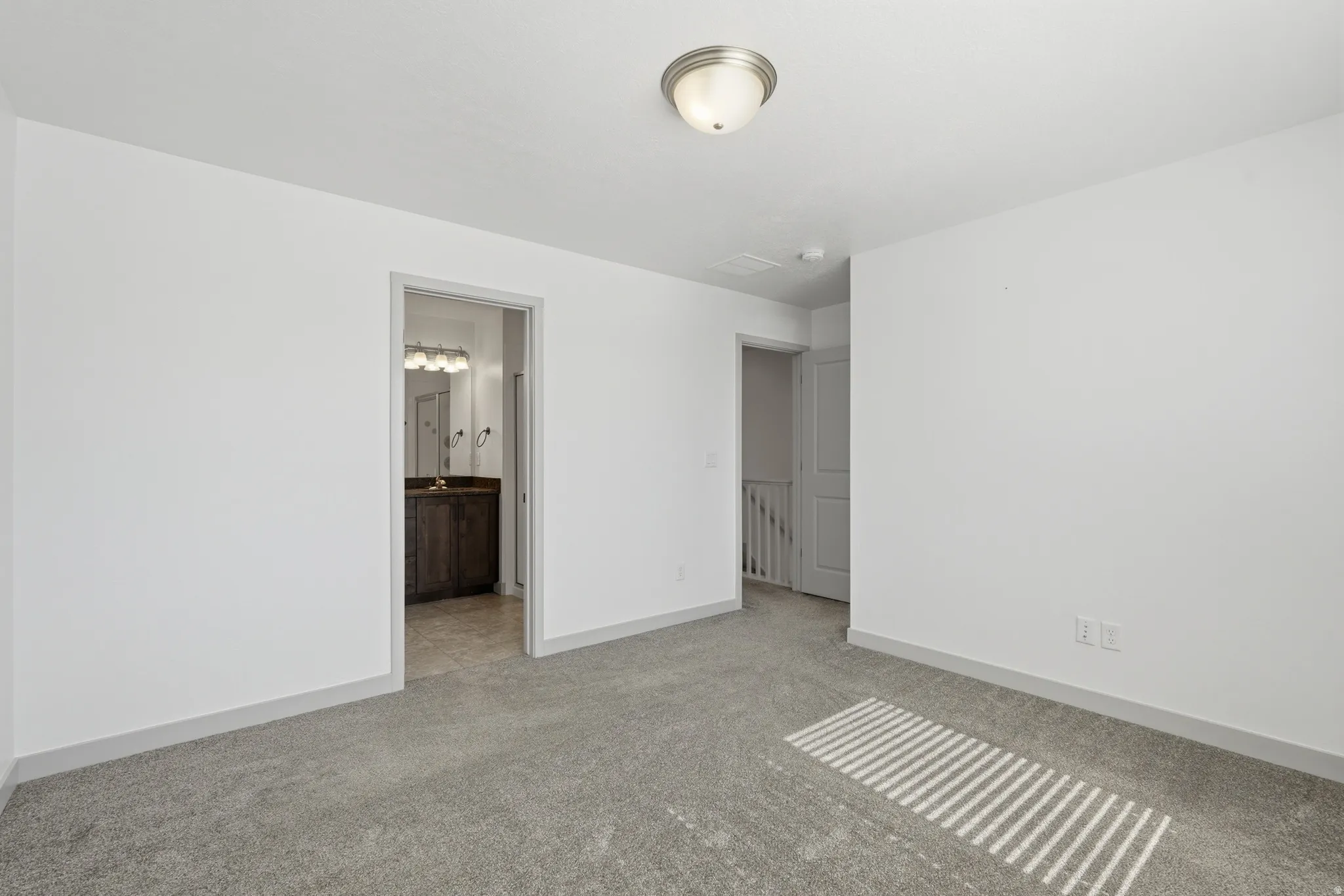Primary bedroom with light colored carpet and ensuite bath