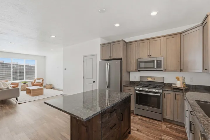 Kitchen featuring stainless steel appliances, dark stone countertops, dark wood finished floors, open floor plan, and a kitchen island