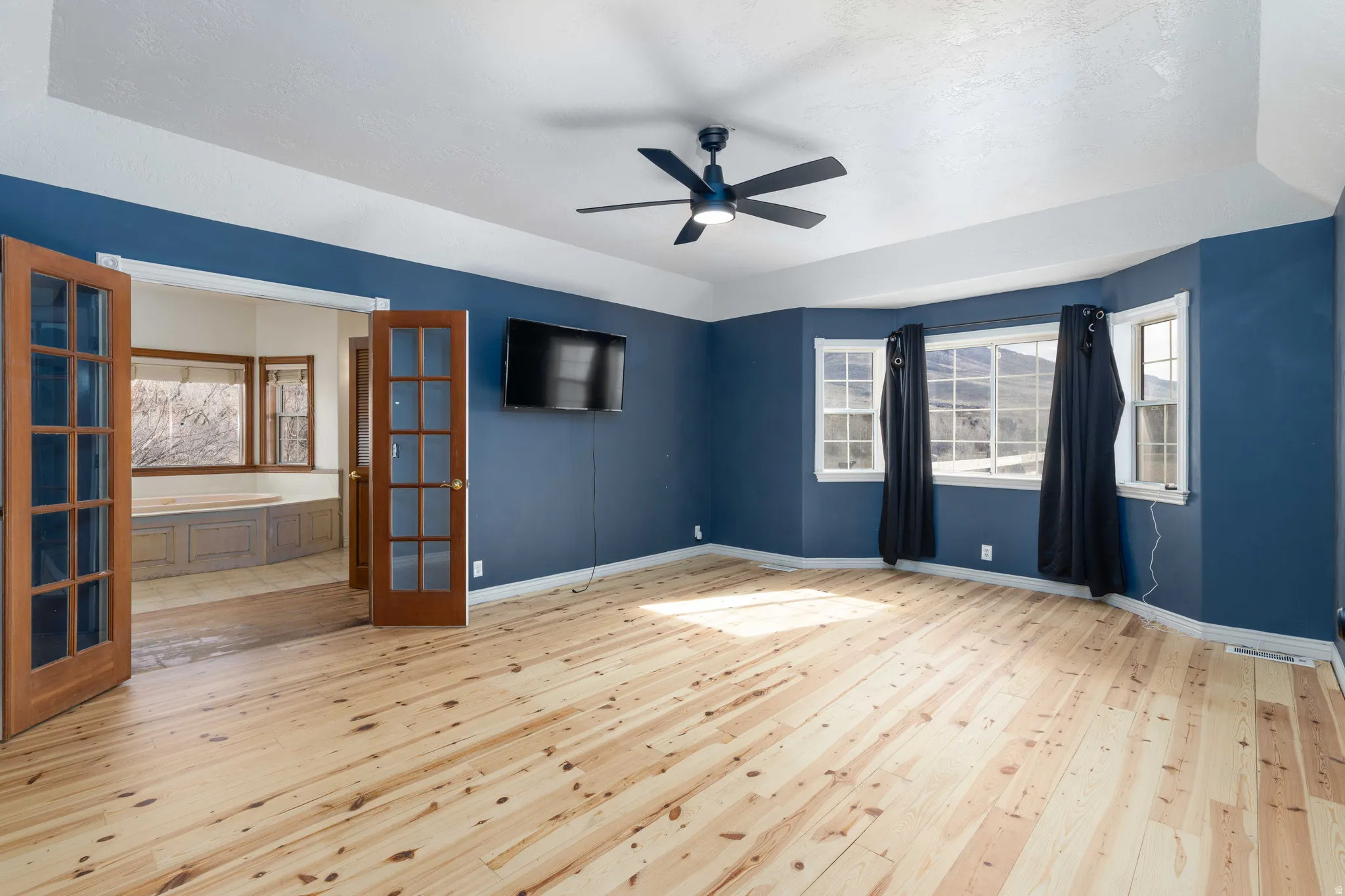 Empty room with light wood finished floors, ceiling fan, and french doors