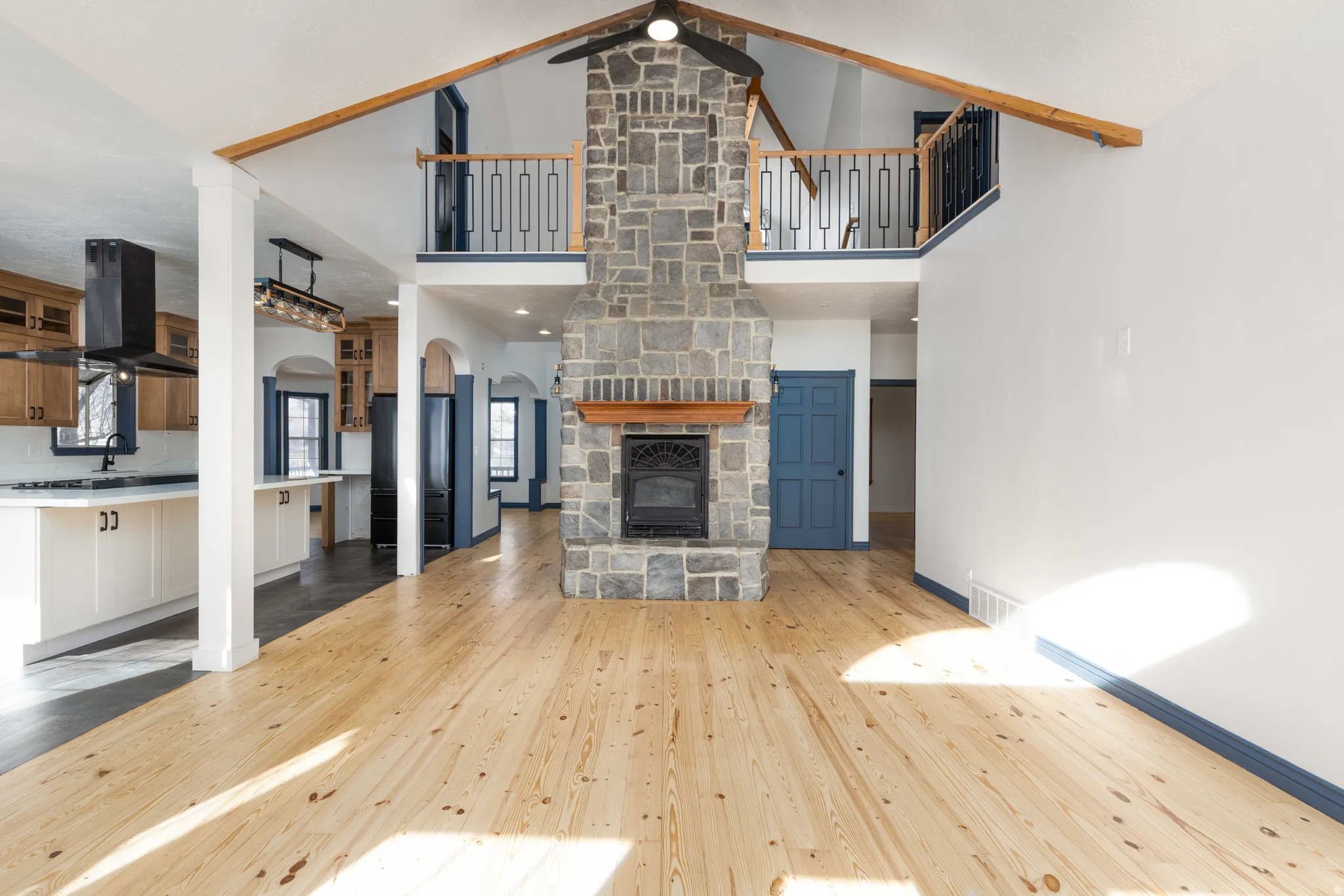 Unfurnished living room with a ceiling fan, a stone fireplace, arched walkways, light wood-style flooring, and lofted ceiling