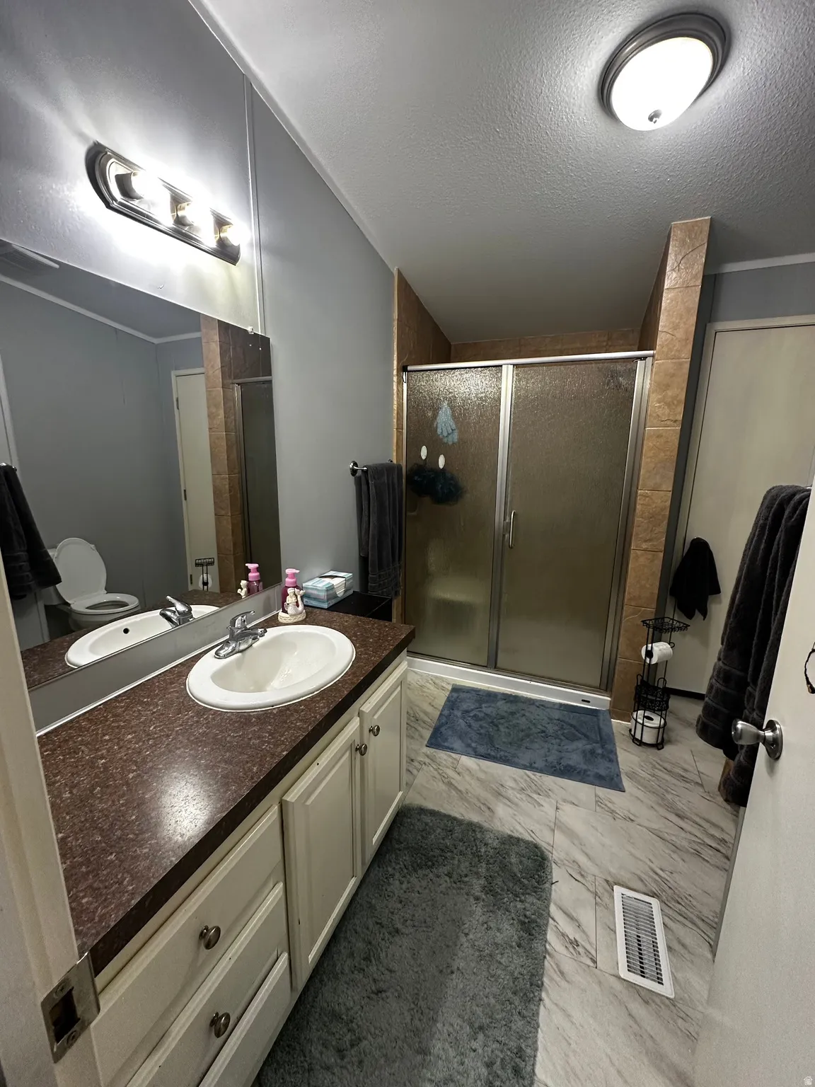 Full bath with vanity, a stall shower, a textured ceiling, and light marble finish floors