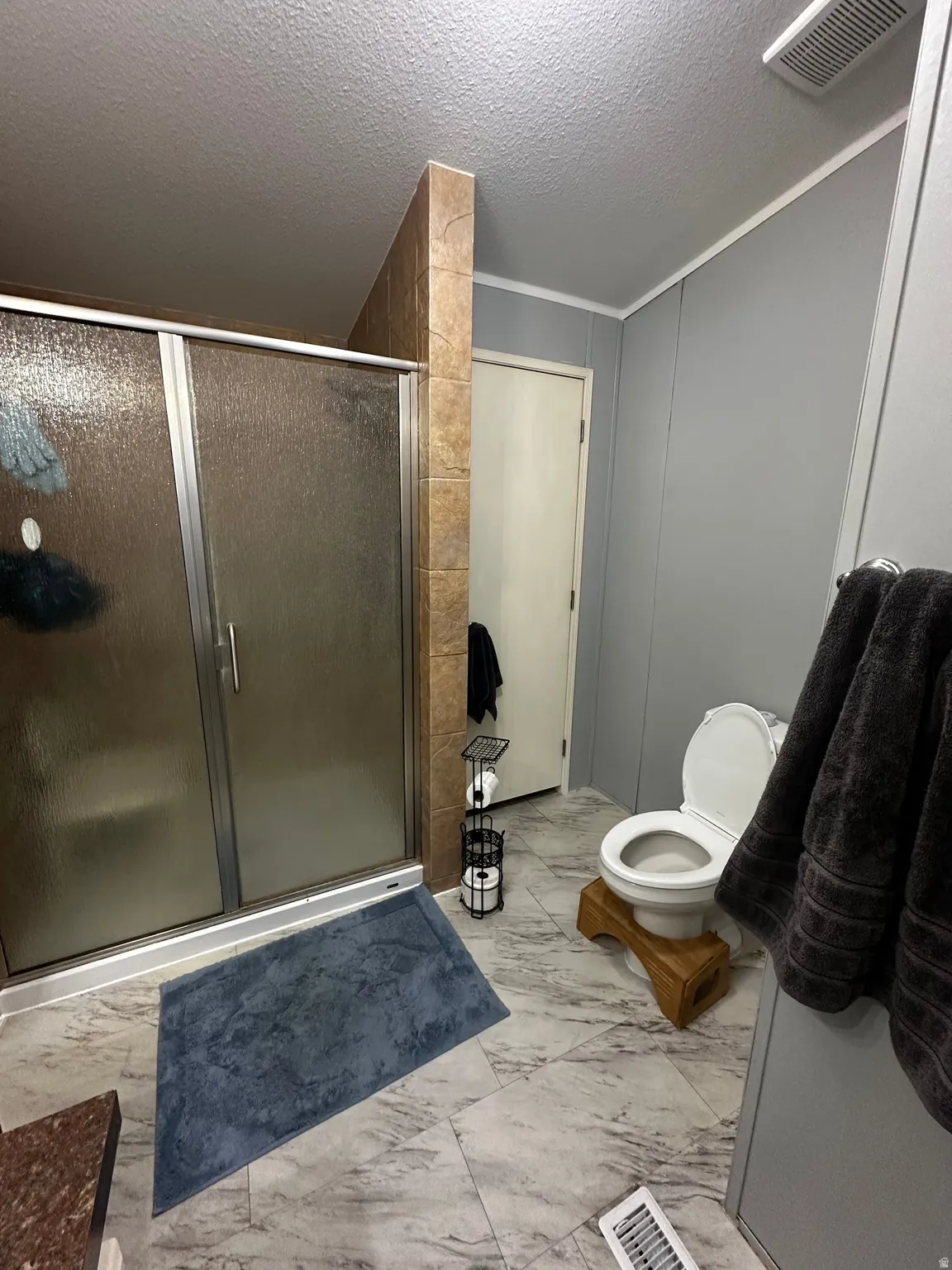 Bathroom featuring a stall shower, a textured ceiling, and light marble finish floors