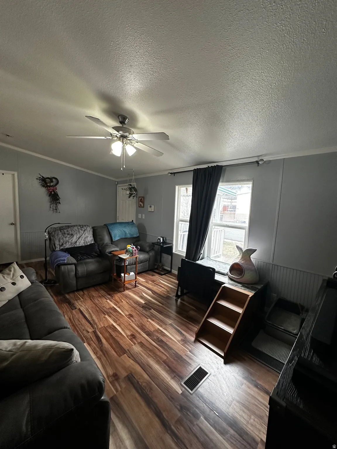 Living room featuring crown molding, dark wood-style floors, a ceiling fan, and a textured ceiling