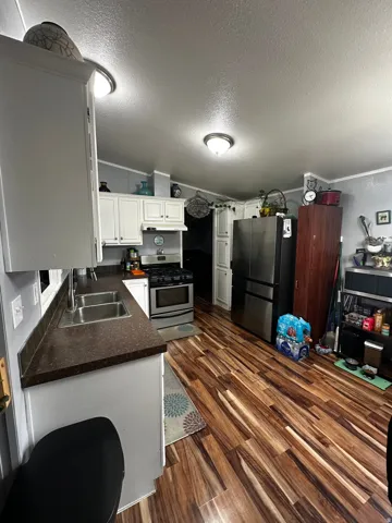 Kitchen featuring dark countertops, white cabinetry, stainless steel appliances, a textured ceiling, and dark wood-style flooring