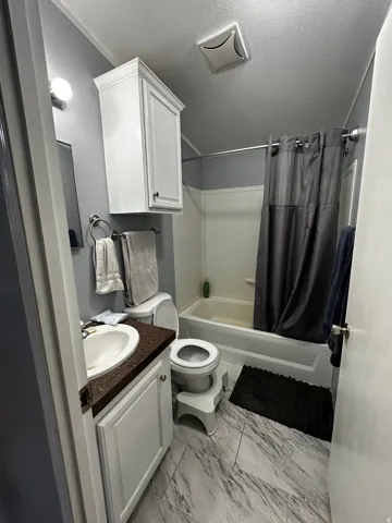 Full bathroom with a textured ceiling, shower / bathtub combination with curtain, vanity, and light marble finish floors