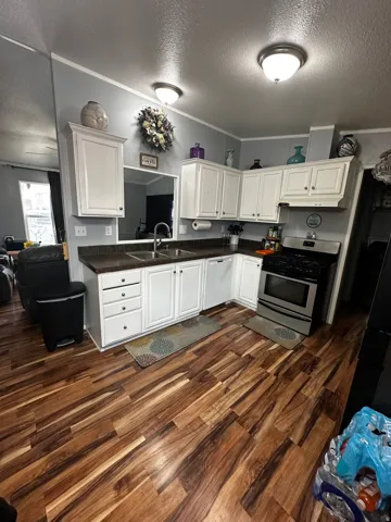 Kitchen with a textured ceiling, stainless steel gas stove, white cabinetry, dark countertops, and dark wood-style floors