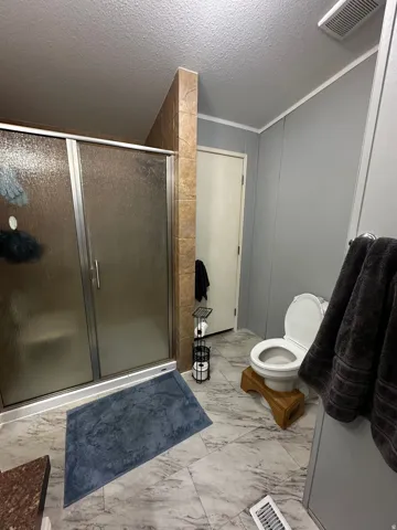 Bathroom featuring a stall shower, a textured ceiling, and light marble finish floors
