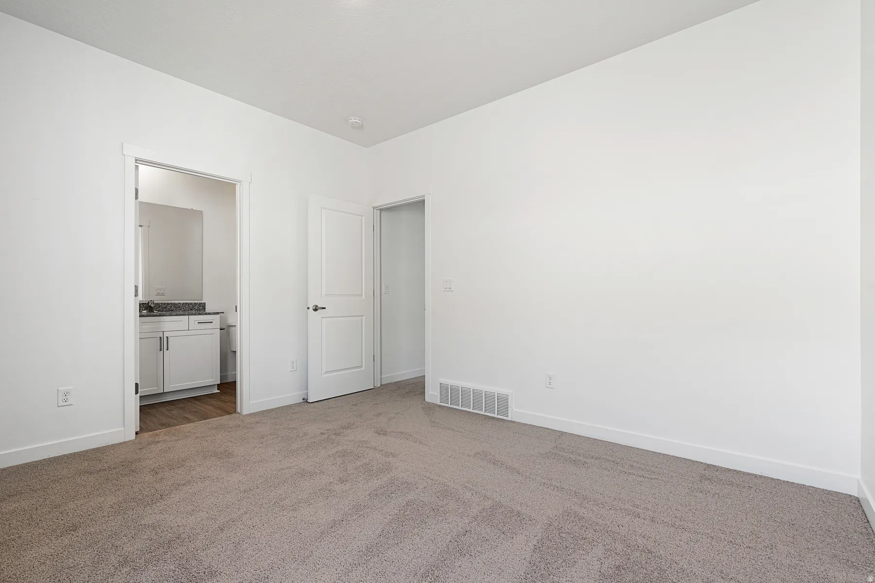 Unfurnished bedroom with dark colored carpet and ensuite bath