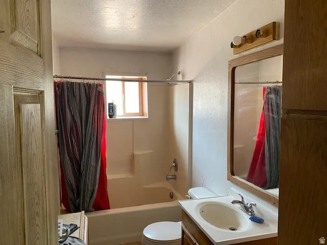 Bathroom with a textured wall, a textured ceiling, vanity, and shower / tub combo with curtain