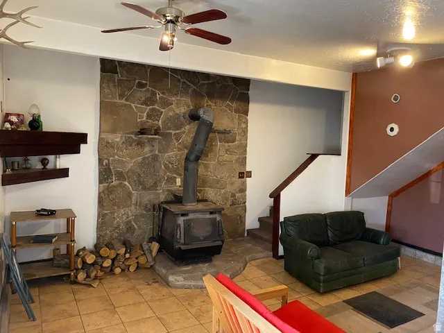 Living area featuring a wood stove, ceiling fan, light tile patterned floors, and a textured ceiling