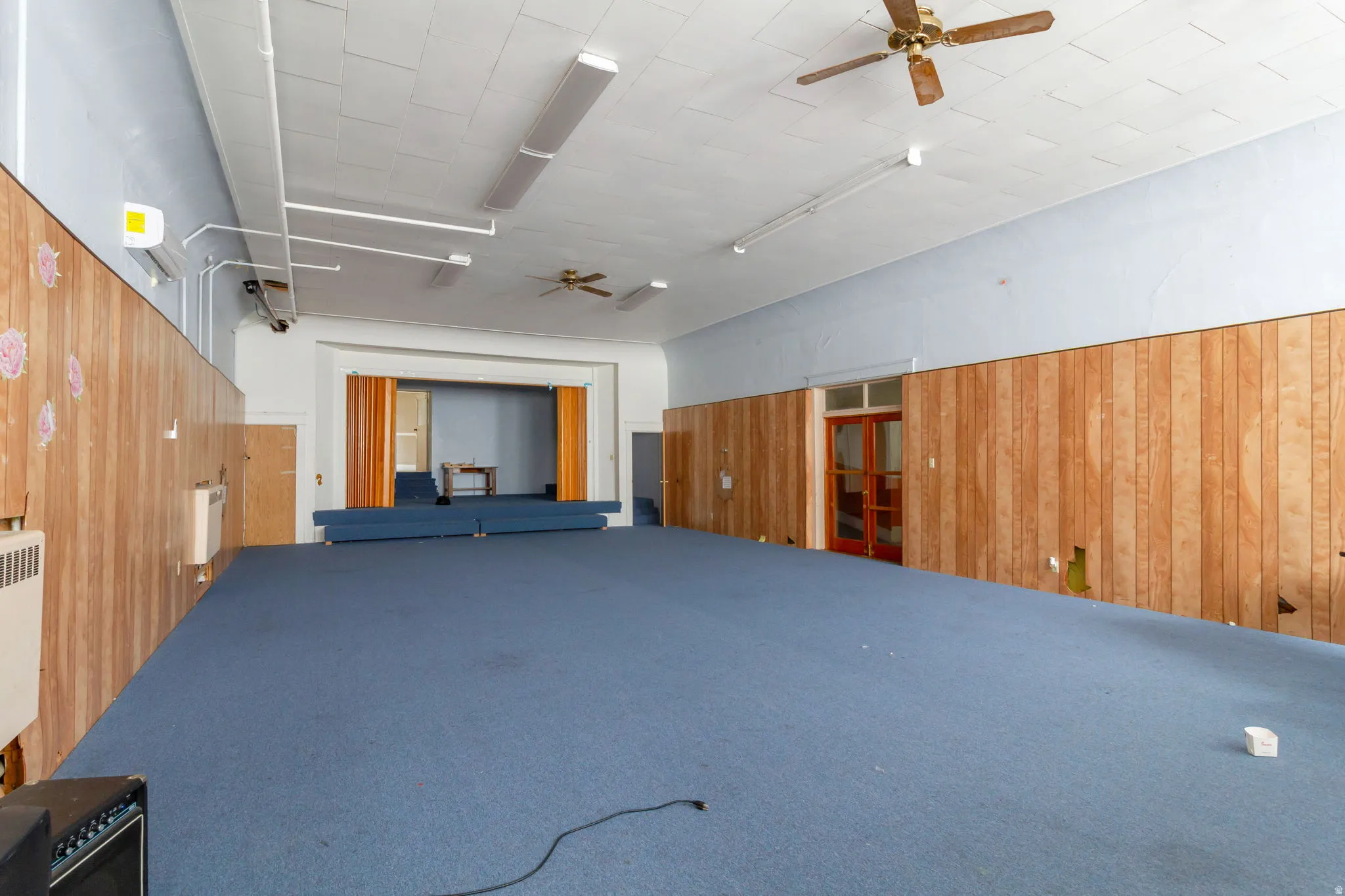 Miscellaneous room with a ceiling fan, wood walls, and carpet
