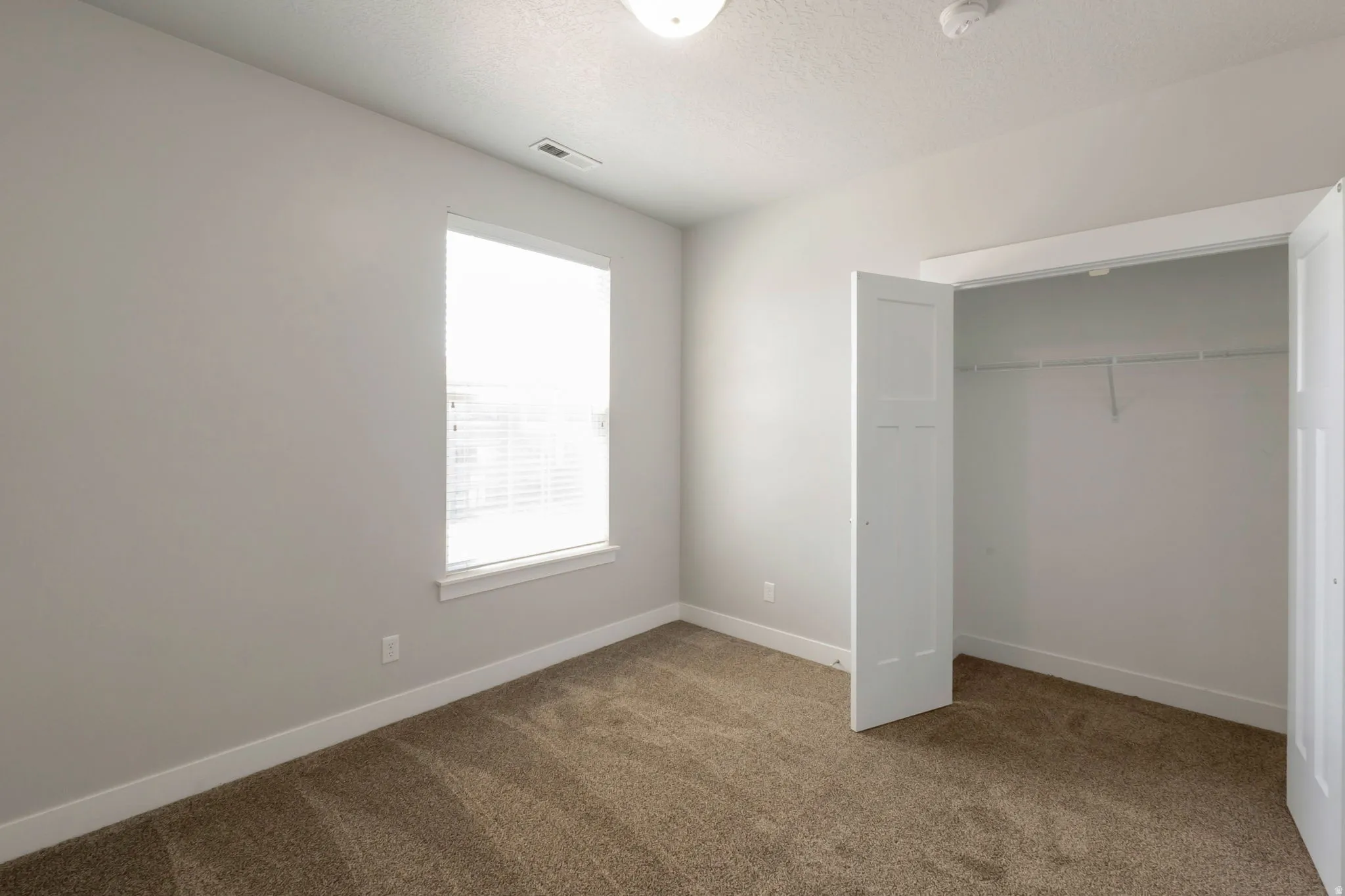 Carpeted room featuring a white window frame, horizontal blinds, and a built-in closet with bifold doors and an organizational system