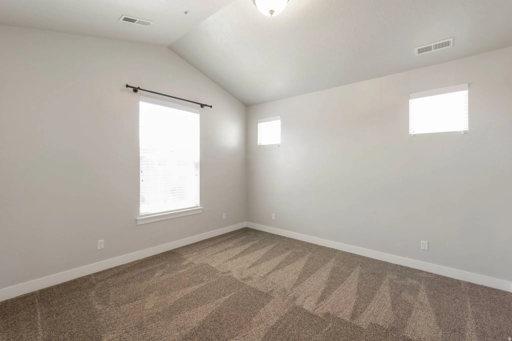 Room featuring a vaulted ceiling, neutral wall tones, and patterned carpeting