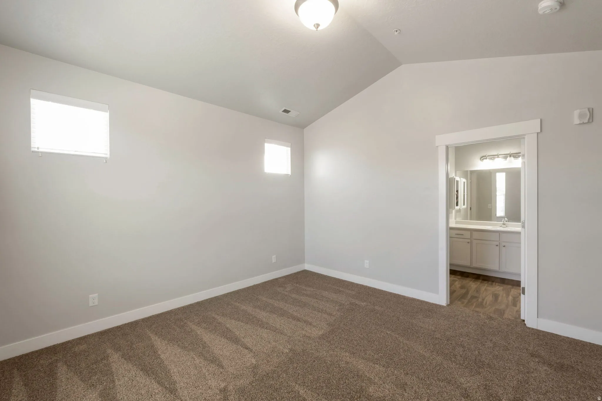 Vaulted ceiling room featuring two windows with horizontal blinds, neutral wall paint, and brown patterned carpeting
