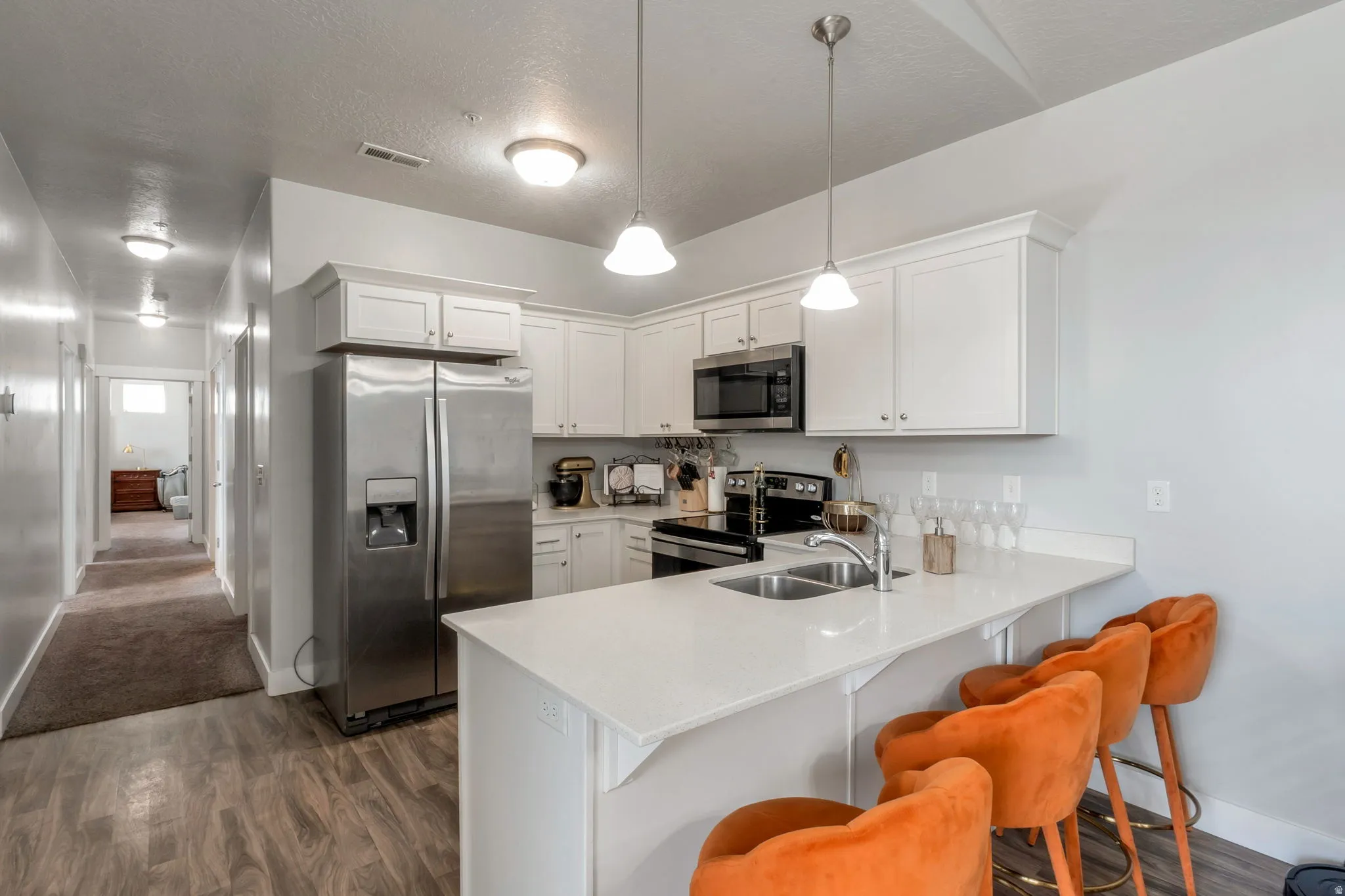 Kitchen with stainless steel appliances, a kitchen bar, a peninsula, white cabinets, and a textured ceiling