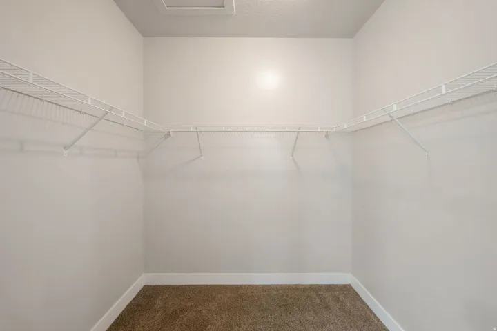 Walk-in closet featuring light beige walls, brown carpet flooring, white baseboards, and white wire shelving