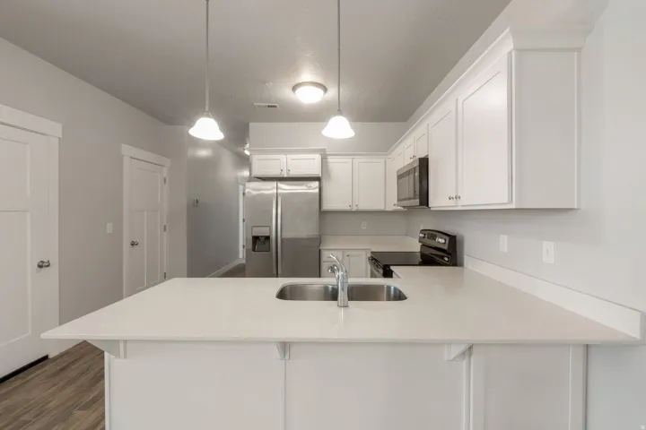 Kitchen featuring a peninsula island with an undermount sink, white cabinetry, stainless steel refrigerator, black range, and built-in microwave