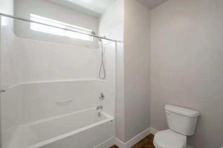 White bathtub and shower combination unit featuring a chrome showerhead with an attached handheld sprayer