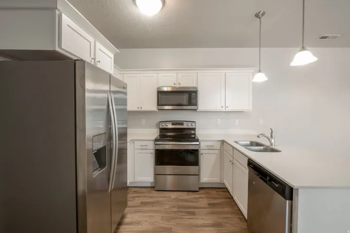 Contemporary kitchen featuring white cabinetry, stainless steel appliances, light-toned countertops, wood-finish flooring, and pendant lighting