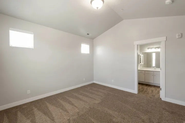 Vaulted ceiling room featuring two windows with horizontal blinds, neutral wall paint, and brown patterned carpeting