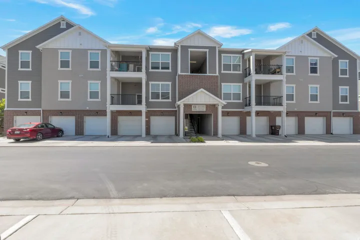 Contemporary multi-story building featuring gray siding, brick accents, white trim, multiple balconies with black railings, and ground-level garages