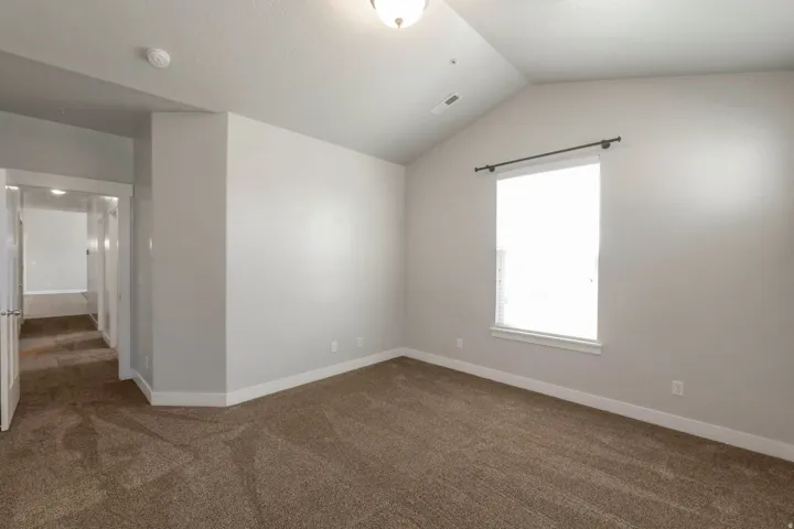 Spacious room featuring vaulted ceilings, a large window with blinds, neutral wall paint, plush carpet flooring, and white trim