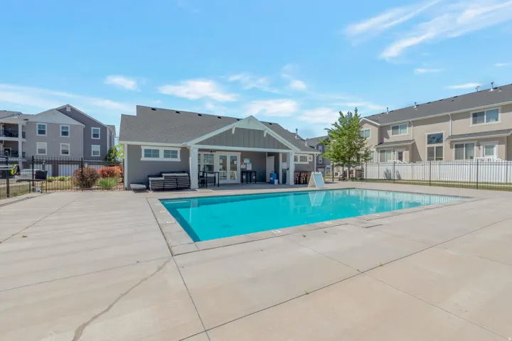 Outdoor swimming pool with a surrounding concrete deck, complemented by a clubhouse building featuring a covered patio area and exterior siding