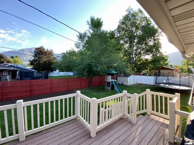 Wooden deck featuring a trampoline, a playground, and a fenced backyard