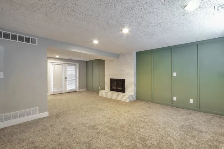Unfurnished living room featuring a decorative wall, a textured ceiling, a brick fireplace, light carpet, and recessed lighting
